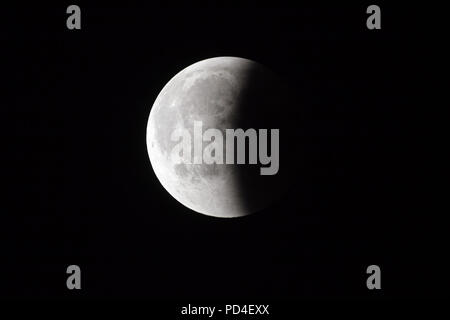 Super sanguinosa luna piena di eclipse fase finale contro il cielo nero sfondo, metà della luna superficie coperta da terra ombra Foto Stock