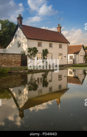 Un cottage è riflessa da un laghetto nel villaggio di vescovo Burton, East Riding of Yorkshire, Regno Unito giovedì 2 agosto 2018, Foto Stock