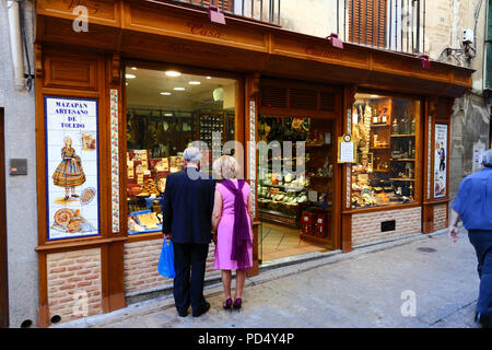 Marito e moglie ben vestiti che guardano dalla finestra del negozio che vende il famoso marzapane locale, Toledo, Castiglia-la Mancha, Spagna Foto Stock