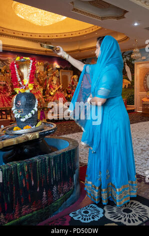 Una donna onde un cero davanti alla statua della divinità Shiva in un tempio indù nel sud Richmond Hill, Queens, a New York. Foto Stock