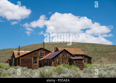 Abbandonata, weathered, legno facciate di edifici e case sotto un bel cielo azzurro con puffy nuvole bianche nella città fantasma di Bodie, California Foto Stock