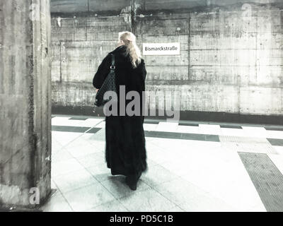 Donna in lungo cappotto di pelliccia nera cammina da sola alla stazione della metropolitana Bismarckstraße, tono urbano malinconico, Berlino Foto Stock