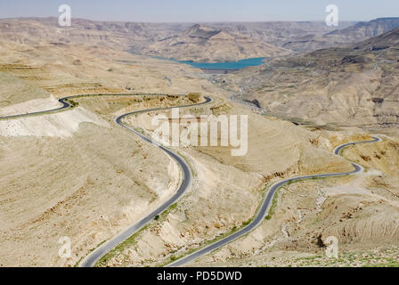 Avvolgimento su strada asfaltata attraverso il deserto e la valle con un lago blu in background Foto Stock
