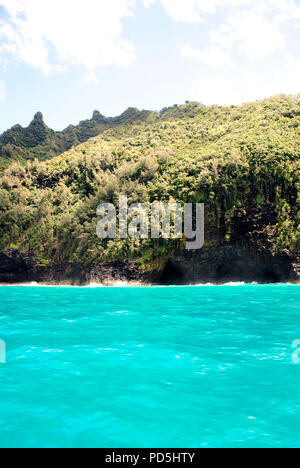 Incredibile turchese brillante di acqua oceanica con lussureggiante foresta verde e costa di roccia e una grotta visto sul Nāpali Coast tour expedition, Kauai, Hawaii, STATI UNITI D'AMERICA Foto Stock