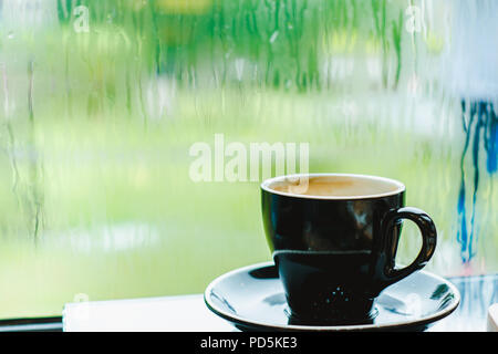Nero caffè tazza sul tavolo nel ristorante cafe vicino alla finestra nel giardino quando piove nel giardino al di fuori del negozio, il cibo e le bevande concetto,uno stile di vita per il tempo libero Foto Stock