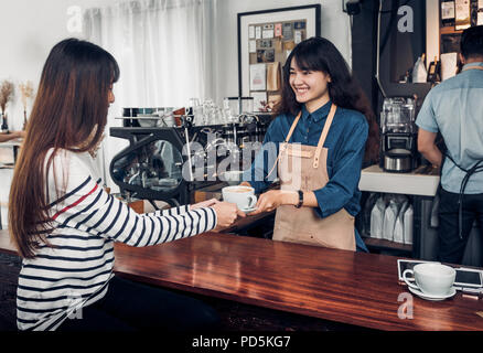 Barista servita calda tazza di caffè per il cliente con un sorriso di fronte al bancone bar nel ristorante cafe,coffee shop business owner concetto,servizio cameriera mente Foto Stock