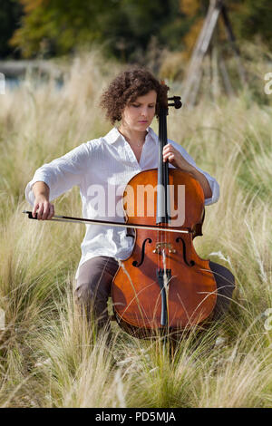 Donna che gioca il violoncello tra i campi Foto Stock