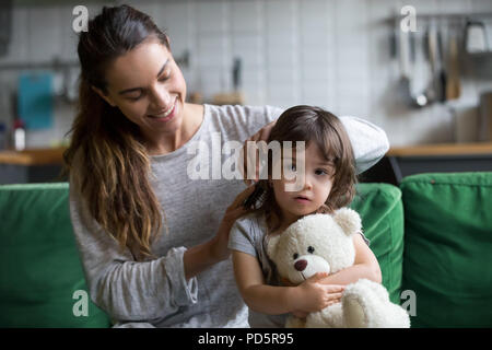 La cura amorevole madre spazzolatura kid figlie capelli seduto sul divano Foto Stock