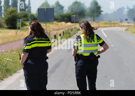 HENGELO, Paesi Bassi - 1 Luglio 2018: due incognite ufficiali di polizia donne guardando un incendio di grandi dimensioni presso il locale di trasformazione di rifiuti di società. Foto Stock