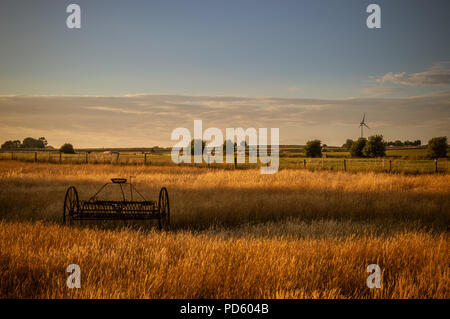 La vecchia e la nuova tecnologia. Il fieno rastrello e la turbina eolica in Staffordshire campo gli agricoltori al tramonto. Foto Stock