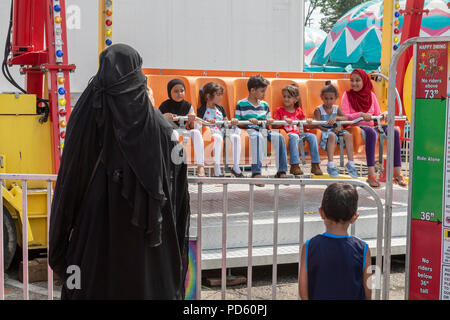 Dearborn, Michigan - una donna in islamica orologi abbigliamento bambini sulla felice carnevale Swing ride presso il Dearborn annuale homecoming festival. Quasi Foto Stock