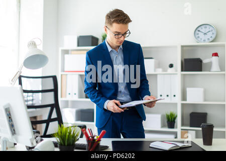 Un giovane uomo sorge nei pressi di un tavolo in ufficio e conserva documenti nelle sue mani. Foto Stock