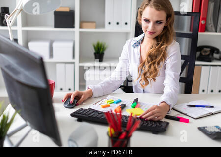 Giovane e bella ragazza seduta alla scrivania in ufficio e lavora al computer. Prima che la ragazza non vi sono documenti. Foto Stock