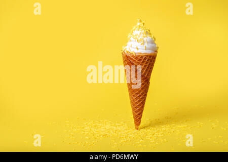 Estate divertente concetto creativo di soft servire il gelato in cono di wafer con un pizzico su sfondo giallo Foto Stock