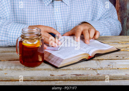 L'uomo la lettura della Sacra Bibbia nonché tè sul tavolo Foto Stock