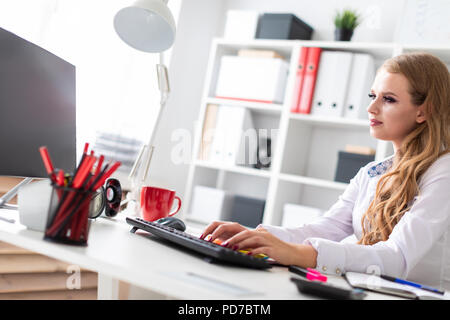 Giovane e bella ragazza seduta alla scrivania in ufficio e lavora al computer. Prima che la ragazza non vi sono documenti. Foto Stock