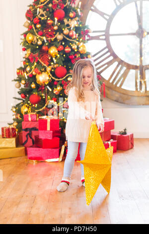 Carino bambina con stella di Natale con albero di Natale sullo sfondo Foto Stock