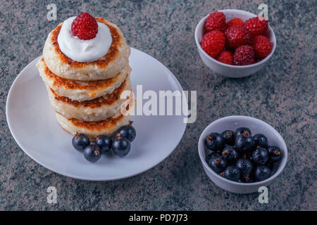 Un mucchio di frittelle con panna e frutti di bosco freschi su uno sfondo di legno Foto Stock