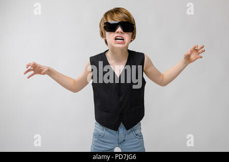 Ritratto di adorabili funny little boy in piedi in studio con occhiali da sole che mostra agression rabbia che vogliono graffio su sfondo grigio Foto Stock