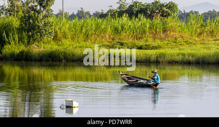 Uomo vietnamita la pesca in Cam Kim nelle acque insulari di mattina in una piccola barca a remi. Foto Stock