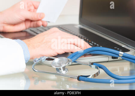 Close up medico con le mani in mano la digitazione su un computer portatile con uno stetoscopio in primo piano Foto Stock