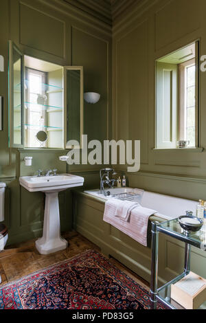 Verde Oliva bagno con pannelli con scaffali di vetro nella finestra alcova e antichi rug Foto Stock