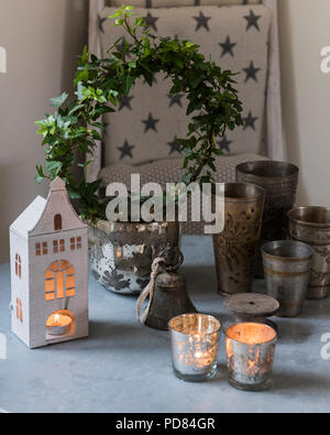 Selezione delle tealight e piccola ghirlanda di edera sul piano del tavolo con coppe in peltro Foto Stock