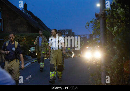 Siegburg Germania. 08 Ago, 2018. Vigili del fuoco a piedi accanto a bruciate le case dopo il fuoco su un terrapieno della linea di ghiaccio vicino a Siegburg. Numerose persone sono state ferite nel fuoco. Credito: Thomas Frey/dpa/Alamy Live News Foto Stock