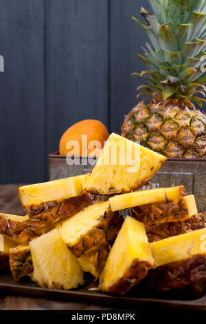 Ananas e pesche in una scatola di metallo su un sfondo di legno. Foto d'epoca. Spazio di copia Foto Stock