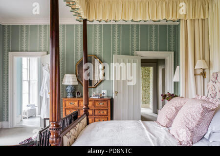 Vintage esagonale specchio sopra botte petto con quattro letto postered una porta aperta alla stanza da bagno ensuite Foto Stock