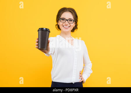 Ritratto di isolato di fiducioso giovane e bella sorridente happy business donna offrendo tazza di caffè su sfondo giallo Foto Stock