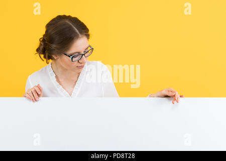 Ritratto di certi belle sorridenti giovane donna di affari che mostra tabellone bianco su sfondo giallo Foto Stock