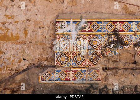 Quattro righe di una parzialmente spezzato tradizionali piastrelle di ceramica su una parete danneggiata di una vecchia casa. El Jadida, Marocco. Foto Stock