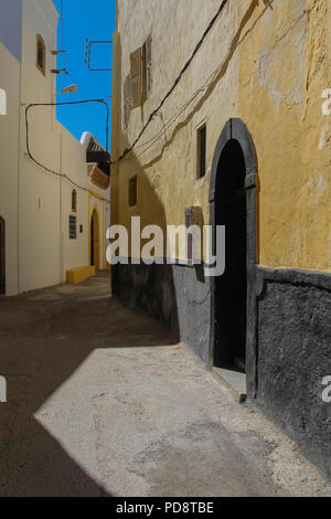 Strada stretta in portoghese ex fortezza. Facciata di colore giallo di una casa sul lato dei diritti. Portoni tradizionali con archi. Azzurro cielo. El Jadida, Mo Foto Stock