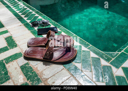 Vista ravvicinata di sandali, un telefono e occhiali da sole su di una piscina del resort Foto Stock