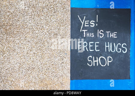 Free Hugs segno sulla parete shop scritti in gesso sulla lavagna nera contro il folle e sfondo blu Foto Stock