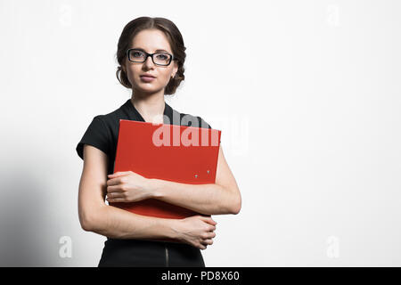 Ritratto di fiducioso giovane e bella donna d'affari di legante di contenimento nelle sue mani in piedi su sfondo grigio Foto Stock