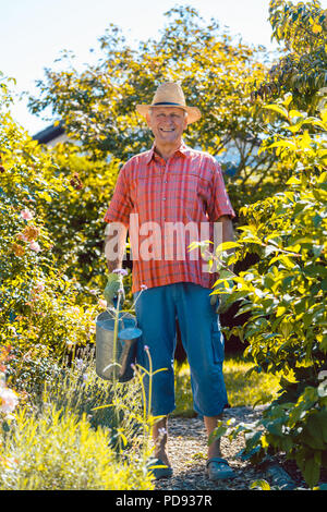 Attivo uomo senior di impianti di irrigazione in giardino in una tranquilla giornata Foto Stock