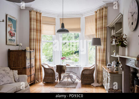 Grande comò in accogliente piano aperto sala colazione con orologio da parete, woodburning stufa e sedie di vimini Foto Stock