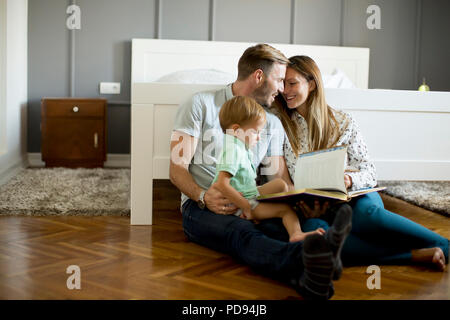 I giovani genitori la lettura di libro a little boy e divertirsi sul floot in camera Foto Stock