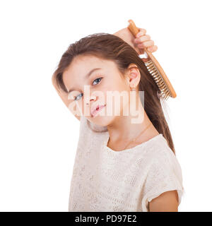 Cura dei capelli concetto con ritratto di poco brunette girl spazzolando la sua indisciplinato, aggrovigliato capelli lunghi isolati su bianco Foto Stock