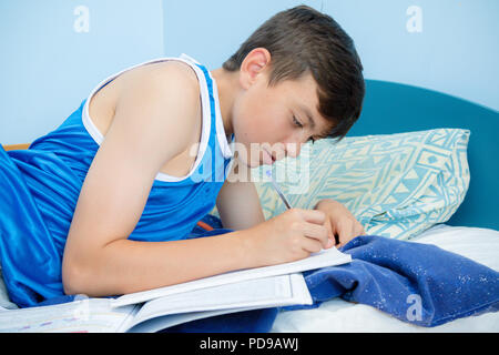 Caucasian ragazzo adolescente posa sul suo letto facendo i compiti di scuola Foto Stock