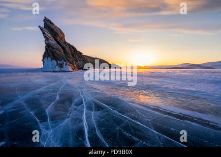 Lago Baikal durante il warm sunrise in inverno. Splendide rocce e crack linee sul ghiaccio. Foto Stock