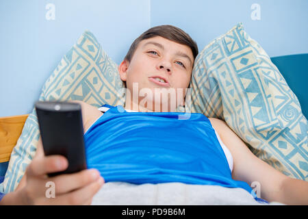 Caucasian ragazzo adolescente sfogliare i canali TV con un telecomando Foto Stock