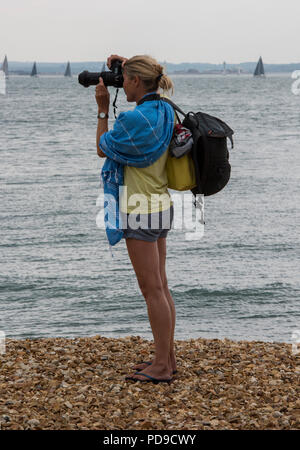 Un attraente giovane donna bionda fotografo in piedi su una spiaggia. Foto Stock