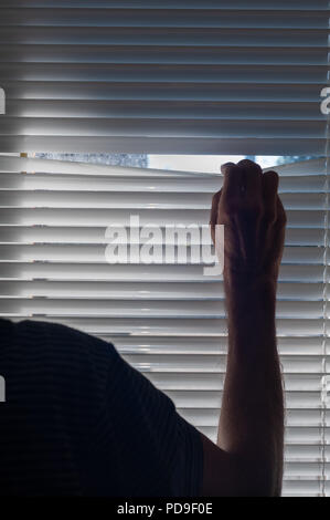 La paura dei visitatori o i chiamanti a freddo uomo di mezza età pigoli attraverso lo spazio di veneziane e guarda fuori per i ladri di cause di disturbo, agorafobia Foto Stock