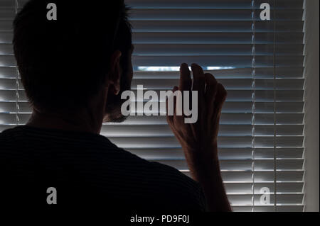 La paura dei visitatori o i chiamanti a freddo uomo di mezza età pigoli attraverso lo spazio di veneziane e guarda fuori per i ladri di cause di disturbo, agorafobia Foto Stock