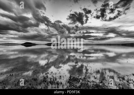 Perfetta e simmetrica nuvole e isole riflessioni su un lago, rendendo le forme astratte Foto Stock