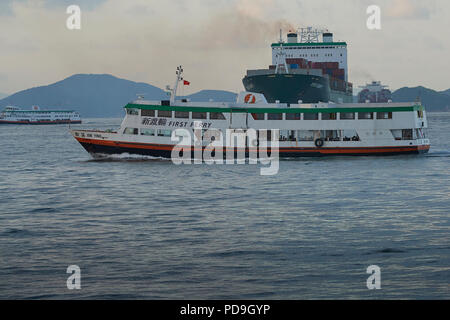 Un traghetto locale attraversa la prua della Evergreen nave portacontainer, mai il dolce, nella trafficata East Lamma canale di spedizione, Hong Kong. Foto Stock