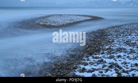 Sfocata onde del mare su una spiaggia di ghiaia ricoperta di neve vicino alla città di Seaton in Devon Foto Stock